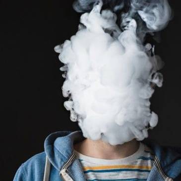 Color photo of young person whose head is a cloud of vape smoke