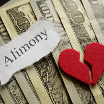 photo of the word "Alimony" typed on a small piece of paper torn out with a small felt broken heart on top of several hundred dollar bills